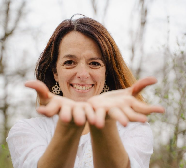 Gesangslehrerin Monica Sardi Frau mit lächelndem Gesicht, die ihre Hände offen und einladend ausstreckt.
